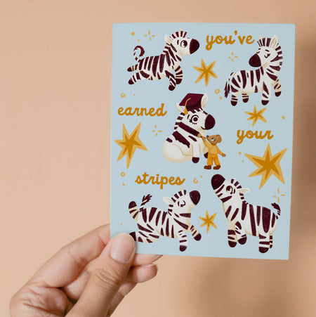 Graduation greeting card featuring stars and joyful zebras surrounding a white horse having it's stripes painted on by a little mouse.