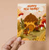 Greeting card with an acorn house, bear, owl, bird, and squirrel in a forest setting with 'Happy New Home!' text.