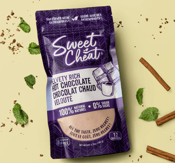Purple packaging of 'Sweet Cheat' hot chocolate with cinnamon sticks and mint leaves on a beige background