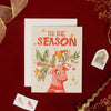 Christmas card with a reindeer illustration and 'Tis the Season' text on a red background. The antlers are tree branches are birds are decorating them with ornaments,