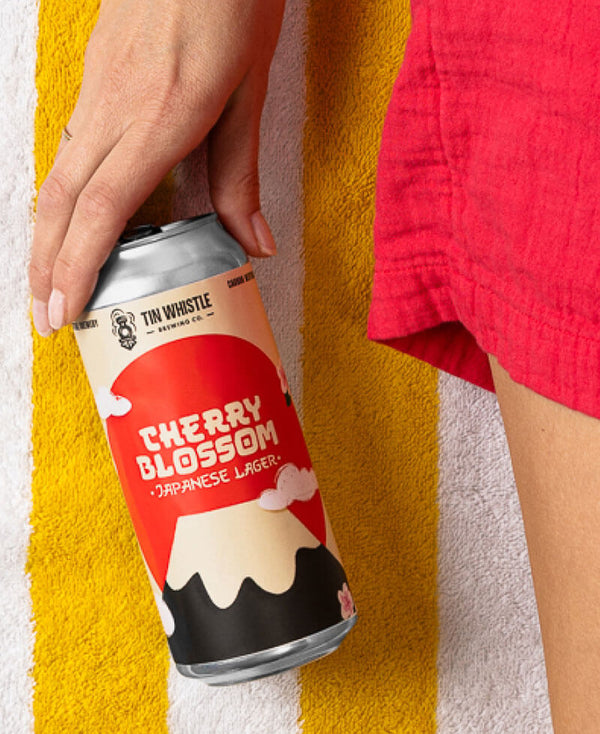 Person holding a can of Cherry Blossom Japanese Lager on a beach towel