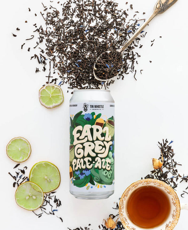 Can of Earl Grey Pale Ale surrounded by tea leaves, lime slices, and a cup of tea on a white background.