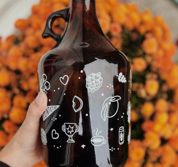 Growler featuring simple, white hand drawn icons being held against a pot of orange plants