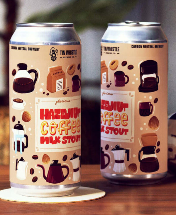 Two cans of Tin Whistle Hazelnut Coffee Milk Stout on a wooden surface.