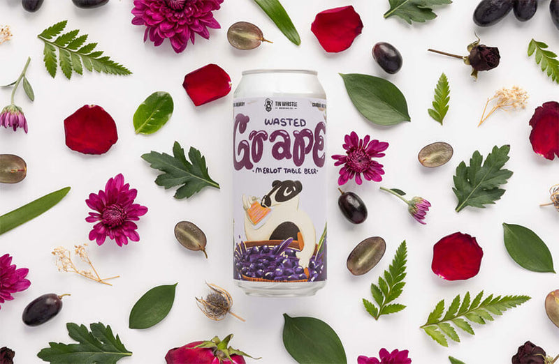Wasted Grape beer can surrounded by flowers and leaves on a white background