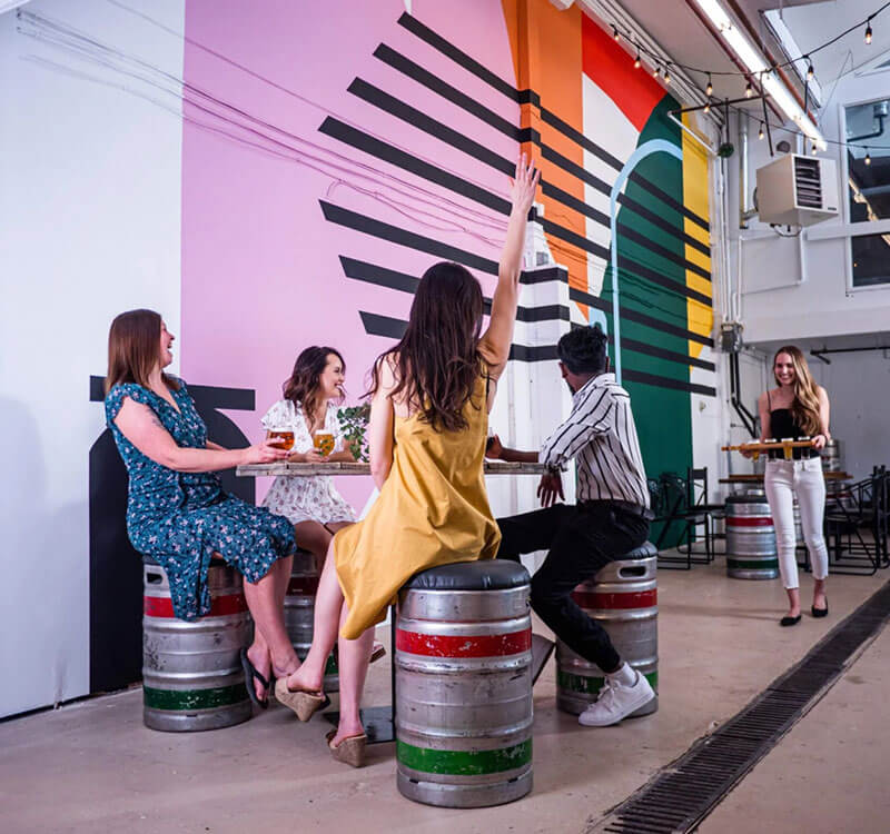 People sitting on kegs in a room with colorful wall art