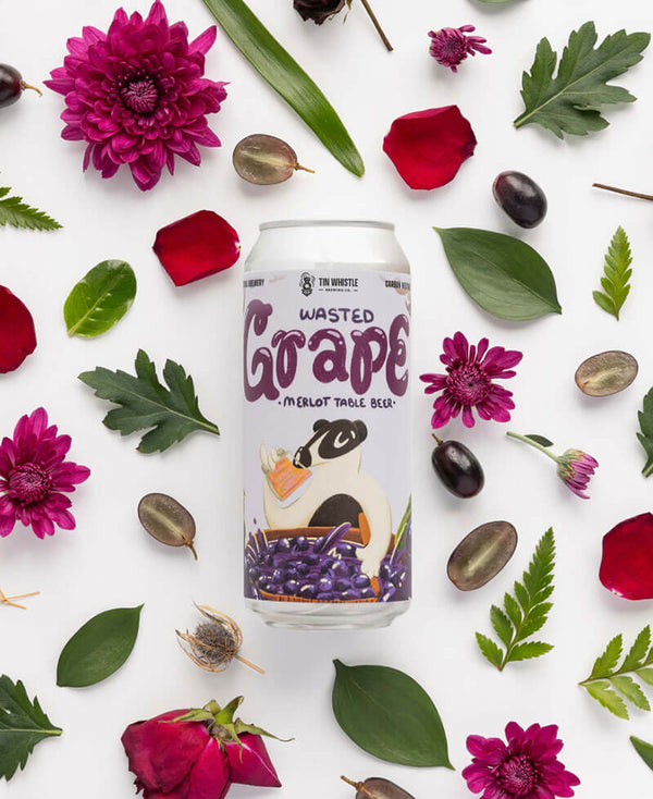 Can of 'Wasted Grape' beer surrounded by flowers and leaves on a white background